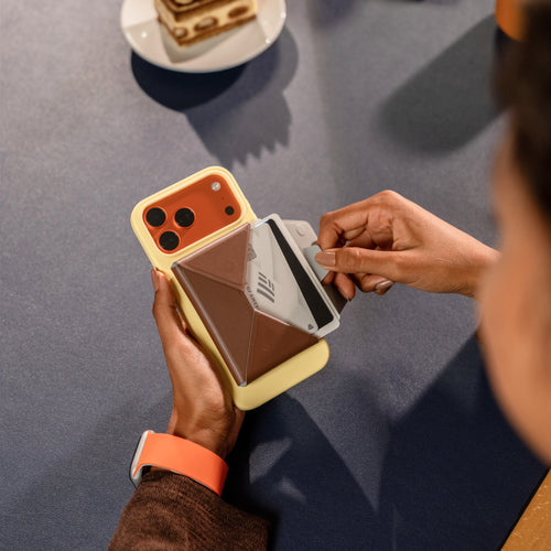 プリンイエロー（黄色）の最新iPhoneケース（iPhone 17）とカカオブラウンのMOFT多機能カードケース＆スタンド。おしゃれな色の組み合わせと、カードをスムーズに取り出す使用シーン。